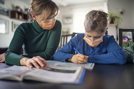 Mom helping son with homework with masks on